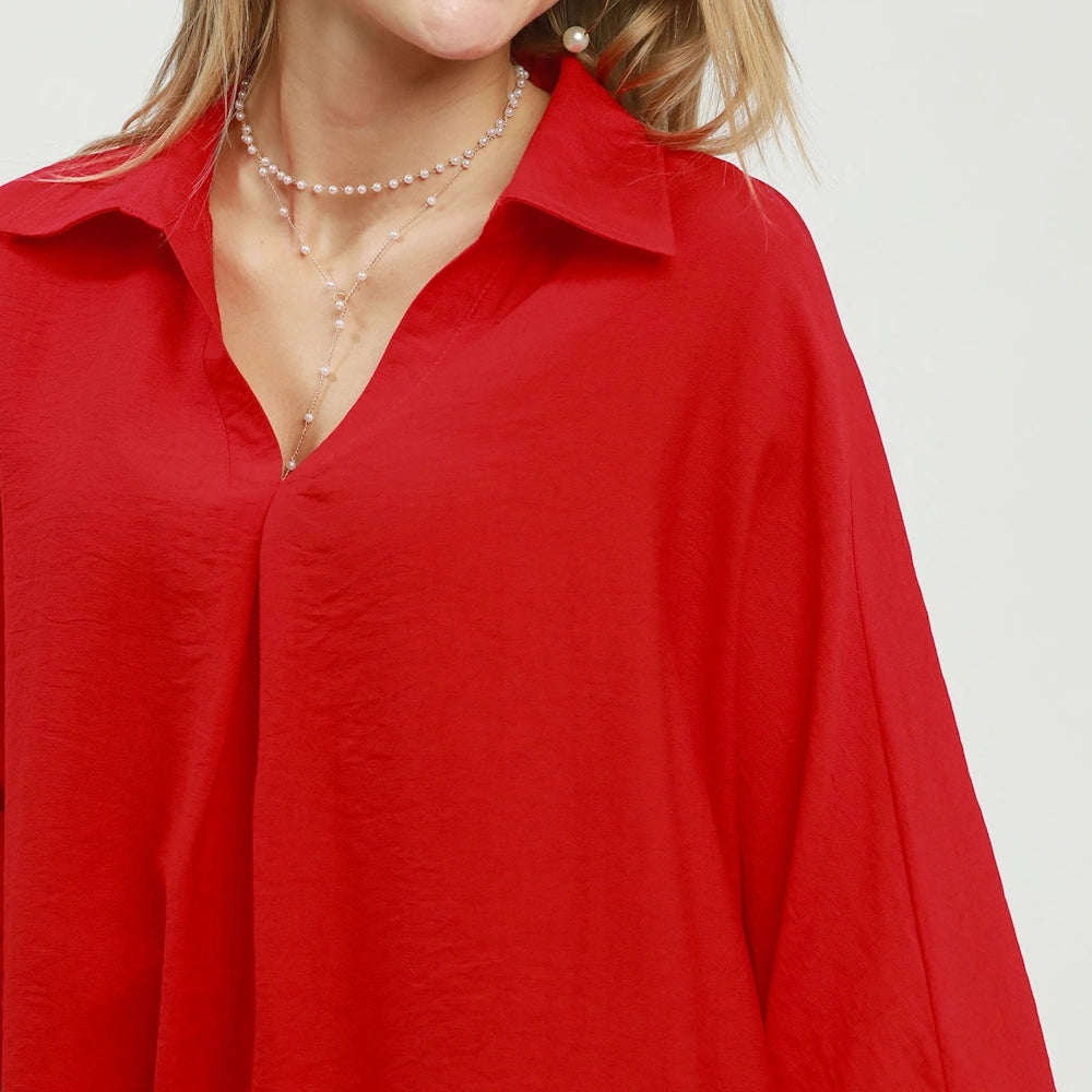 Woman wearing a vibrant red oversized button-up shirt and a delicate silver pearl necklace.