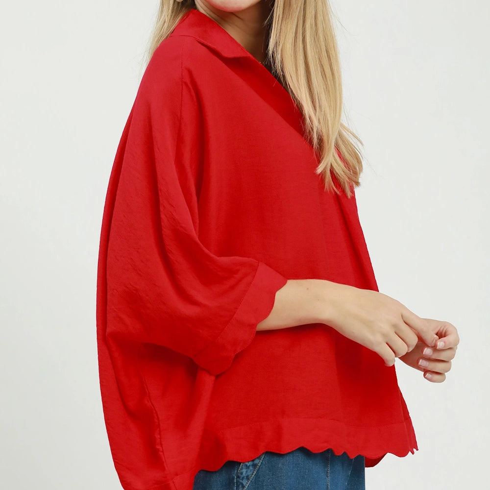 Side view of a vibrant tomato red collared top with wide sleeves and a detailed scallop hem.
