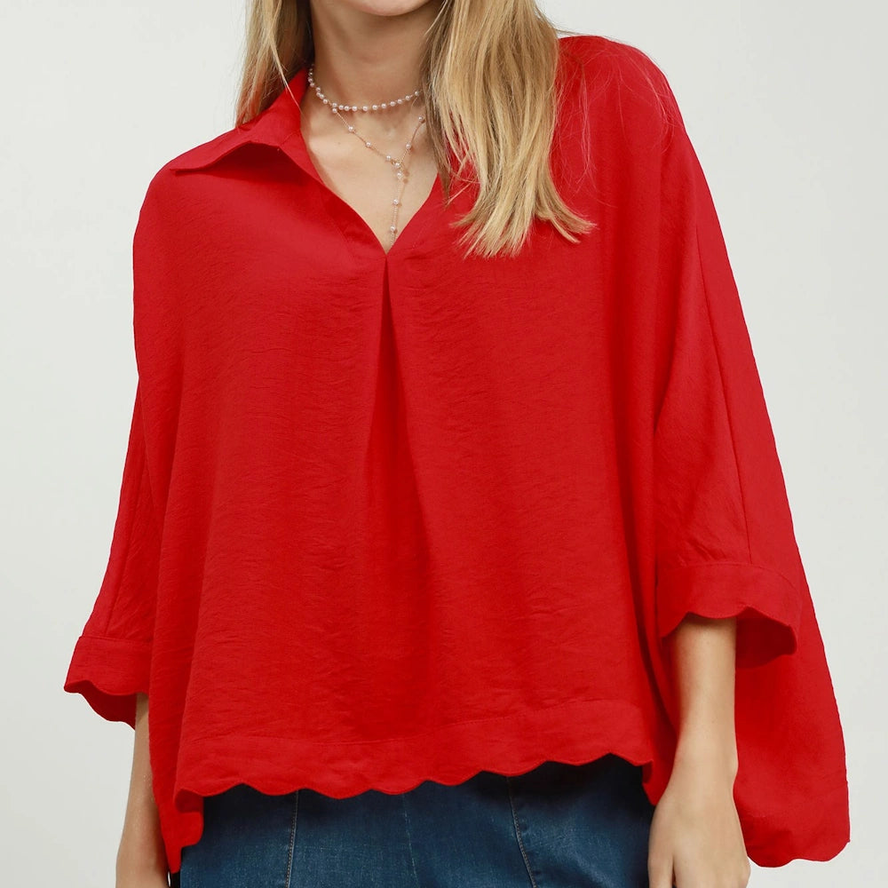 Woman in a tomato red collared top with a scalloped hem and loose sleeves.