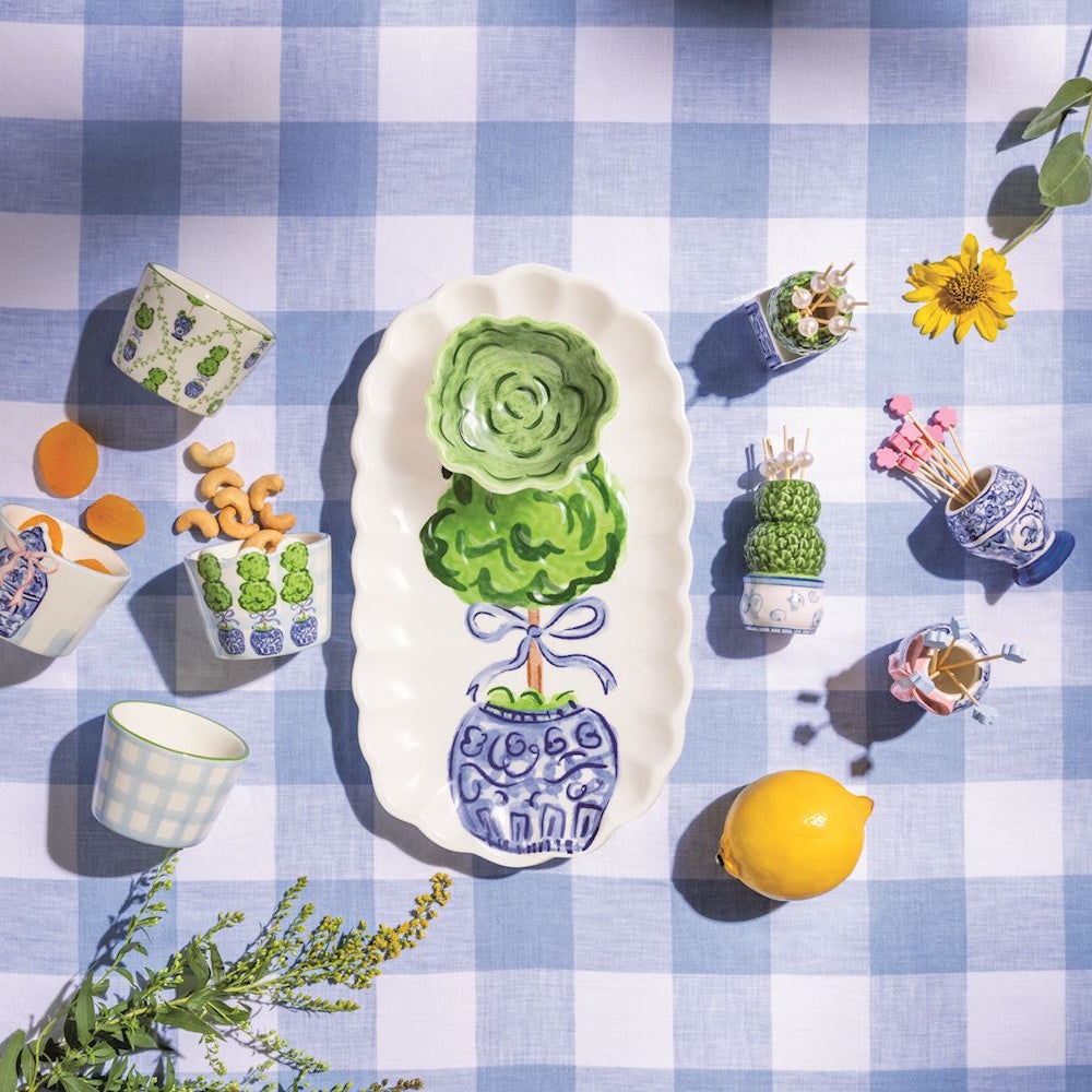 Blue and white topiary themed serving platters, bowls, and toothpick holders on a blue checkered tablecloth.