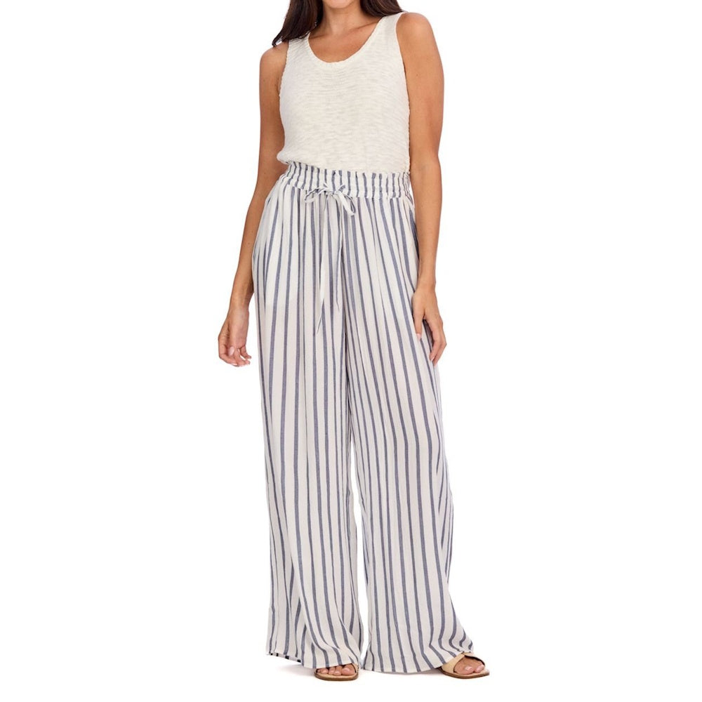 Woman in a white sleeveless top and wide-leg, blue and white striped drawstring pants with sandals.