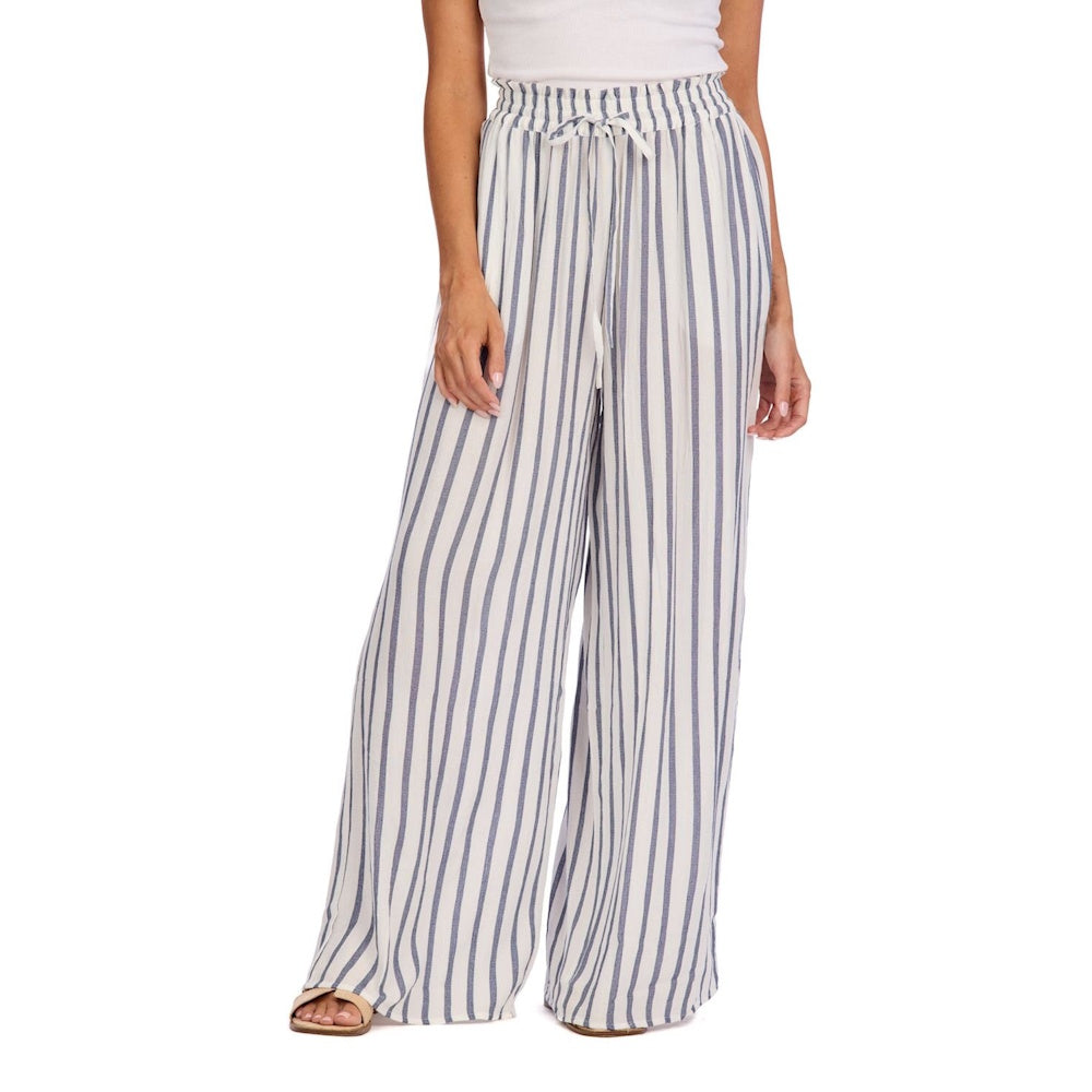 Woman wearing high-waisted, wide-leg beach pants with blue and white vertical stripes and a drawstring waist.
