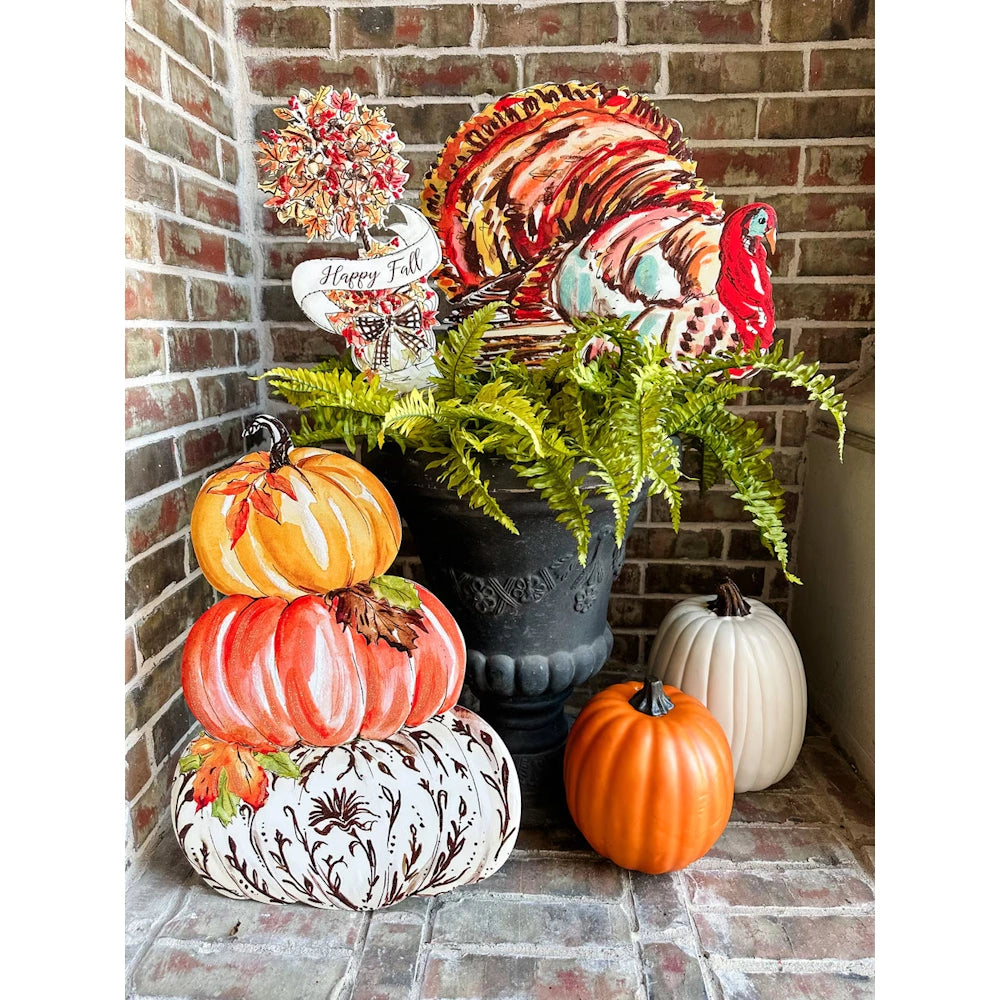 Fall porch display with a colorful turkey sign in a fern planter and a stack of painted pumpkins.