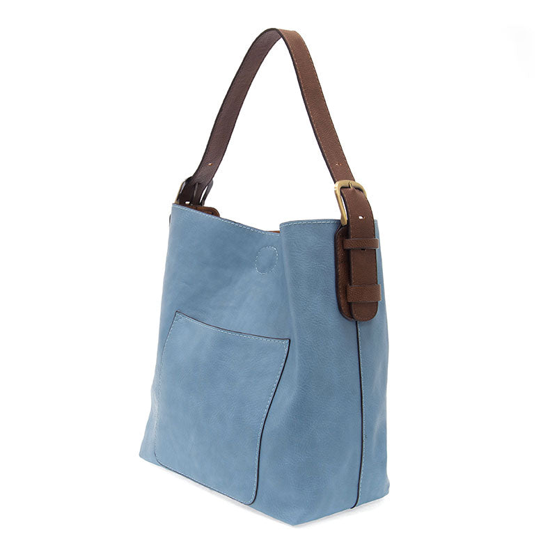 Light blue faux-leather hobo bag with a brown shoulder strap and brass hardware, featuring an open front pocket.