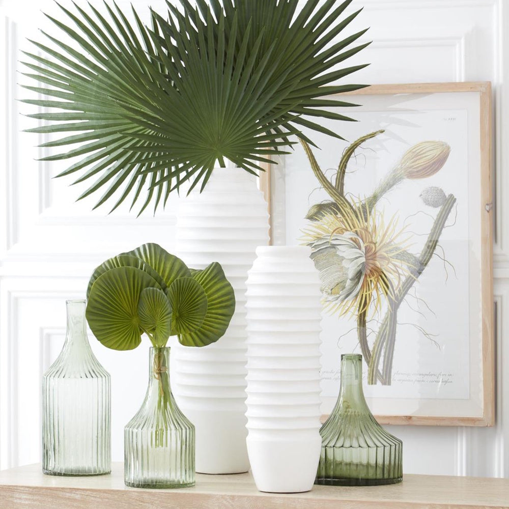 Green and white ribbed glass and ceramic vases with palm leaves and botanical wall art.