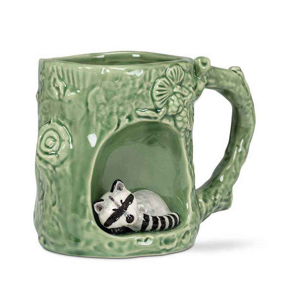 Green ceramic tree trunk mug with a small raccoon sleeping inside a hollow base, branch-shaped handle.
