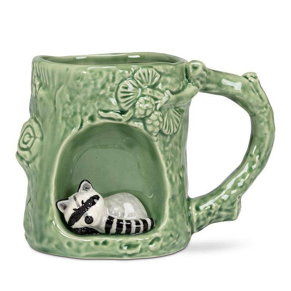 Green ceramic tree trunk mug with branch handle featuring a small sleeping raccoon figurine inside a hollow.