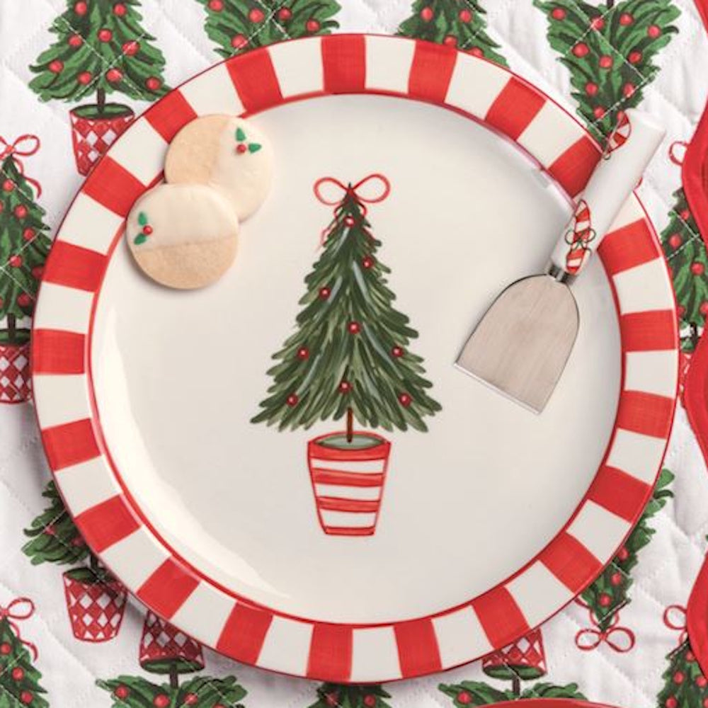 Red-striped Christmas plate with topiary tree illustration, cookies, and spatula on patterned mat.