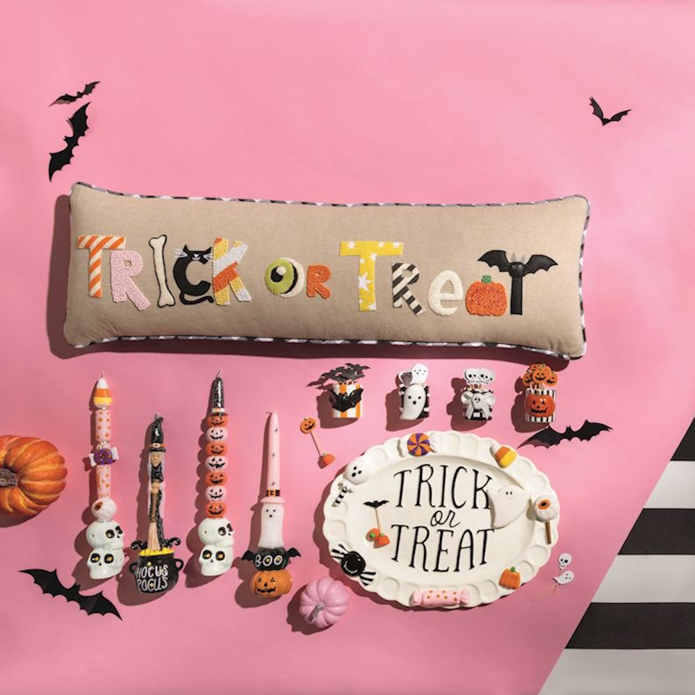 A long Trick or Treat lumbar pillow arranged with Halloween candles and a matching platter on a pink background.