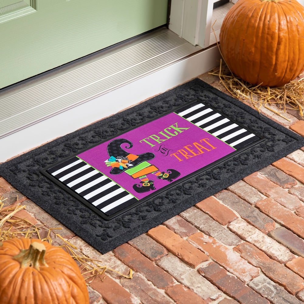 Purple witch doormat insert placed in a dark gray scroll-patterned mat frame on a brick porch.