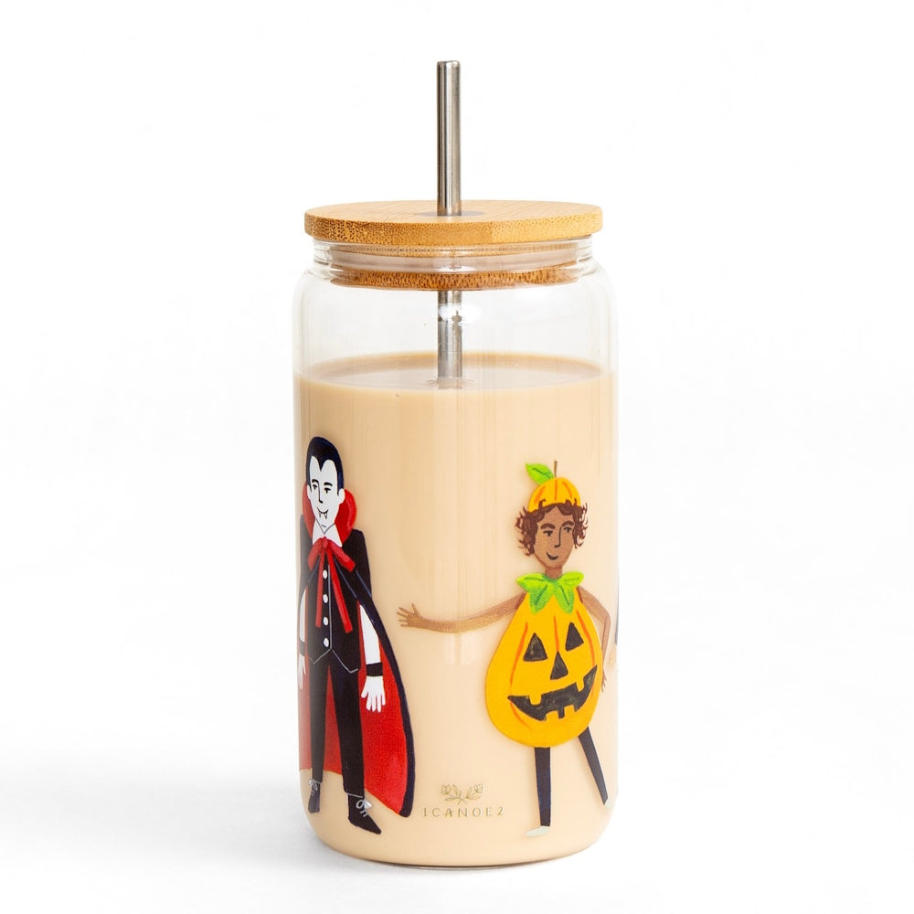 A glass can tumbler filled with iced coffee, decorated with trick-or-treaters in Halloween costumes.