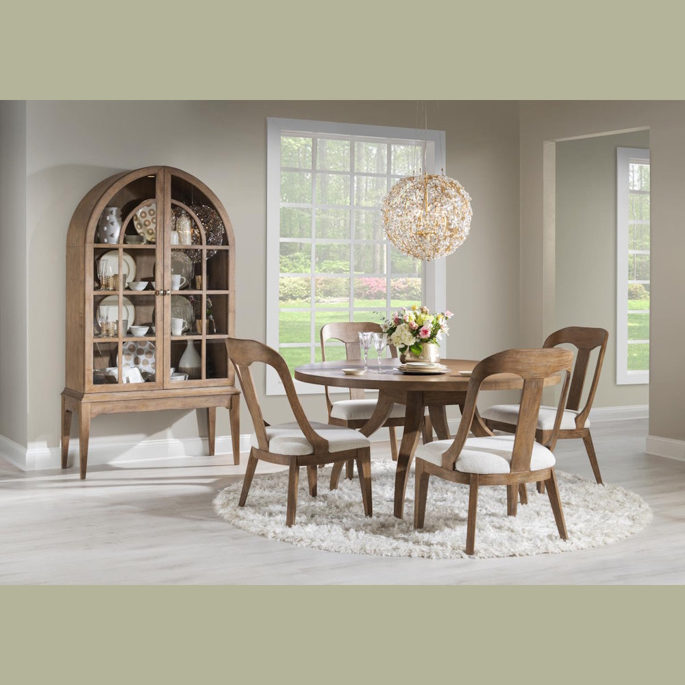 Round wood dining table set with upholstered chairs, arched hutch, and crystal chandelier.