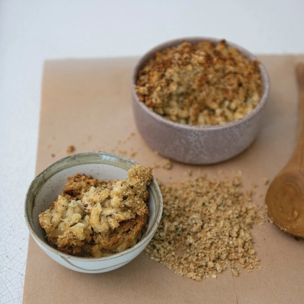 Two bowls of baked macaroni and cheese topped with seasoned breadcrumbs, served next to extra breadcrumbs.