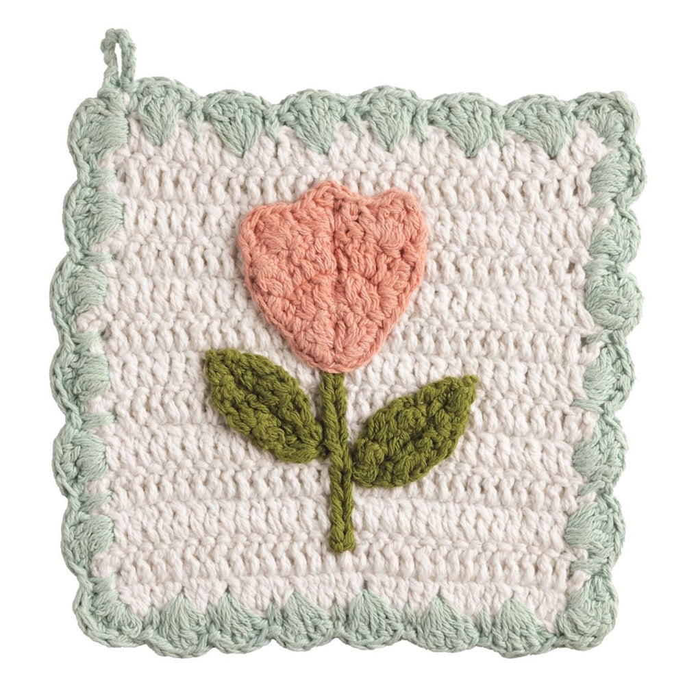 Handmade crochet tulip pot holder with a scalloped green border and a pink flower on a white textured background.