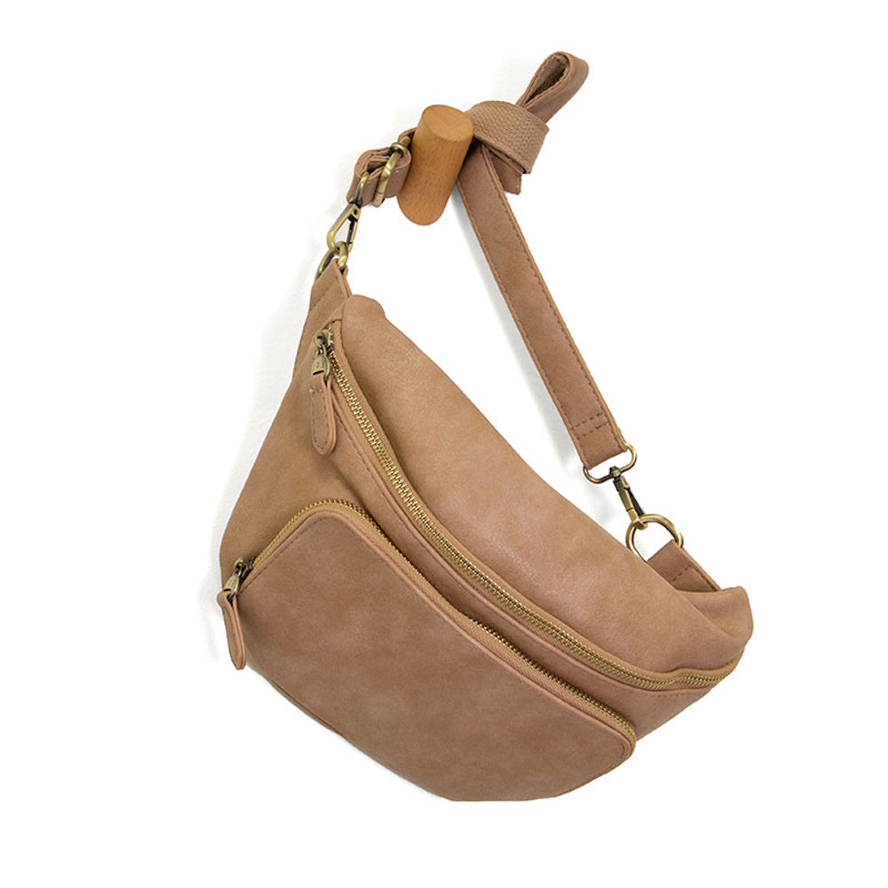 Tan vegan leather fanny pack with gold zippers and adjustable strap hanging on a wooden wall peg.