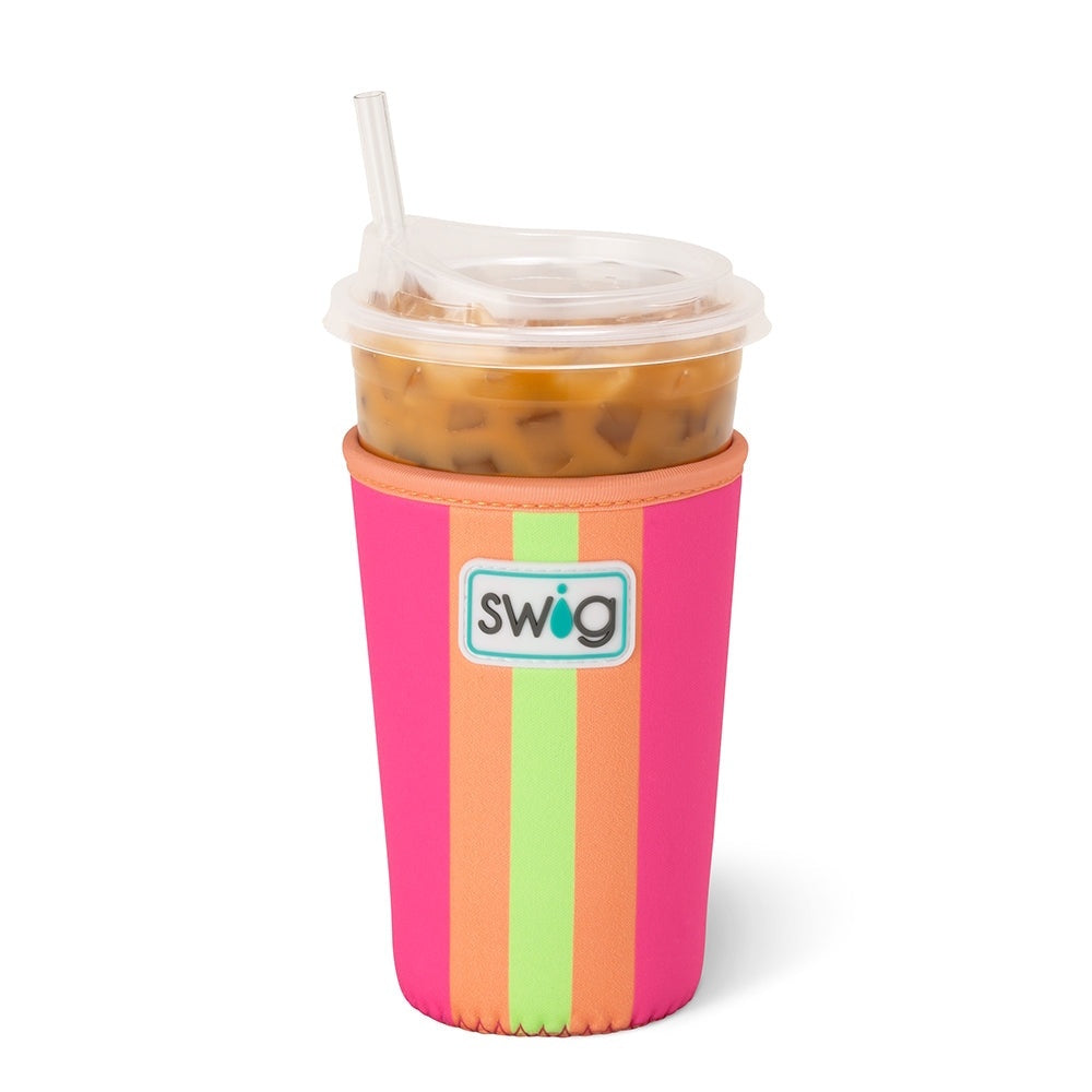 An iced coffee cup in a bright pink, orange, and green striped Swig insulated sleeve with a clear lid and straw.