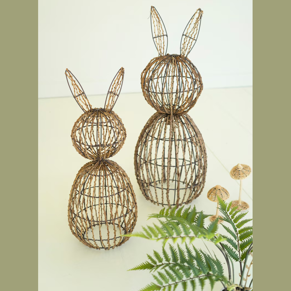 Two rustic twig and iron wire rabbit topiary frames in varying sizes next to a green fern and small woven mushrooms.