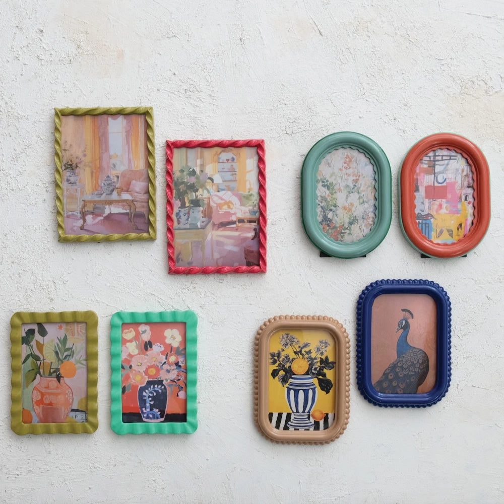Collection of colorful textured photo frames in various shapes including twisted, beaded, and ruffled designs on a white wall.