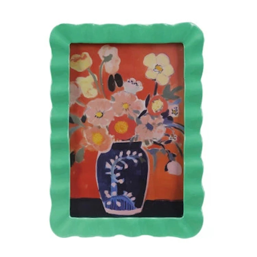 Vibrant floral art in a green scalloped picture frame featuring a blue vase with colorful flowers on an orange background.