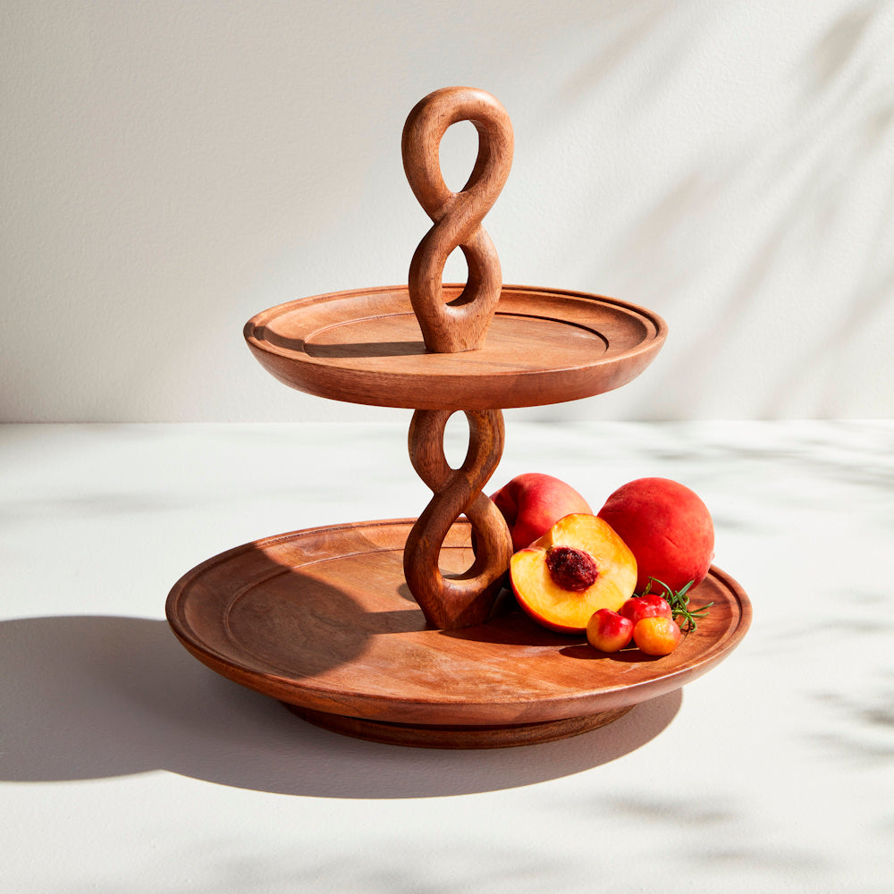 Wooden 2-tier serving tray with a twisted infinity-style handle, displaying fresh peaches on a white surface.