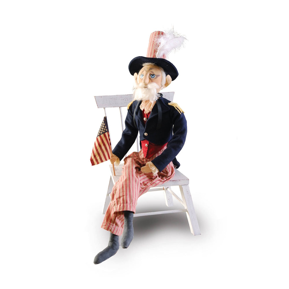 Handcrafted Uncle Sam art doll in patriotic attire, seated on a white chair and holding a small American flag.