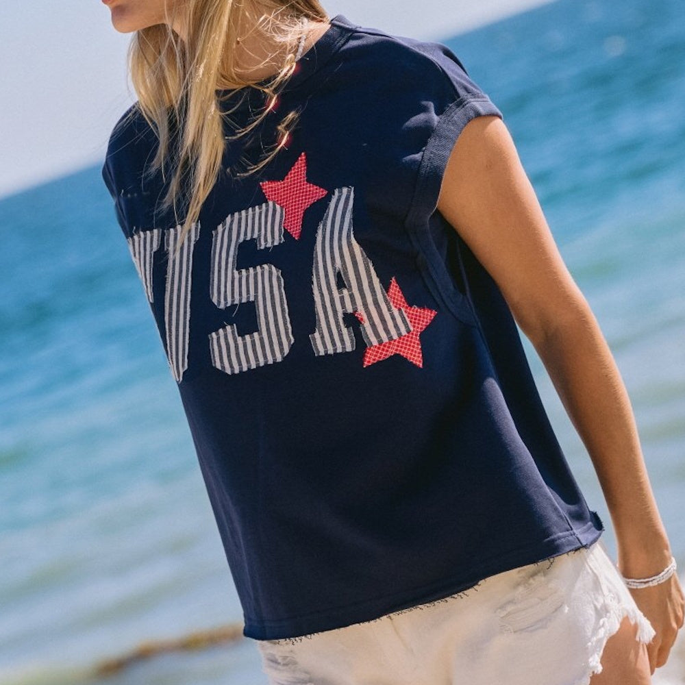 Side view of a person wearing a navy USA muscle tank with striped letters and red stars by the ocean.