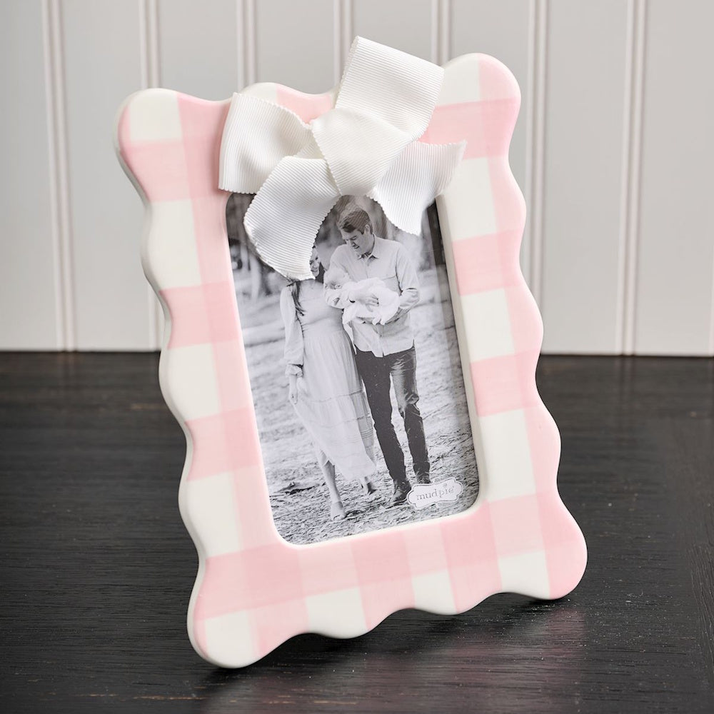 Pink gingham scalloped ceramic picture frame with white bow and family photo on a dark wood surface.