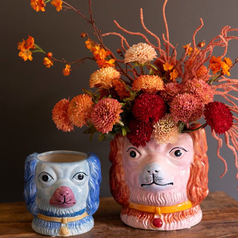 Two vintage-style ceramic dog head vases in blue and pink, with the pink vase holding orange and red flowers.