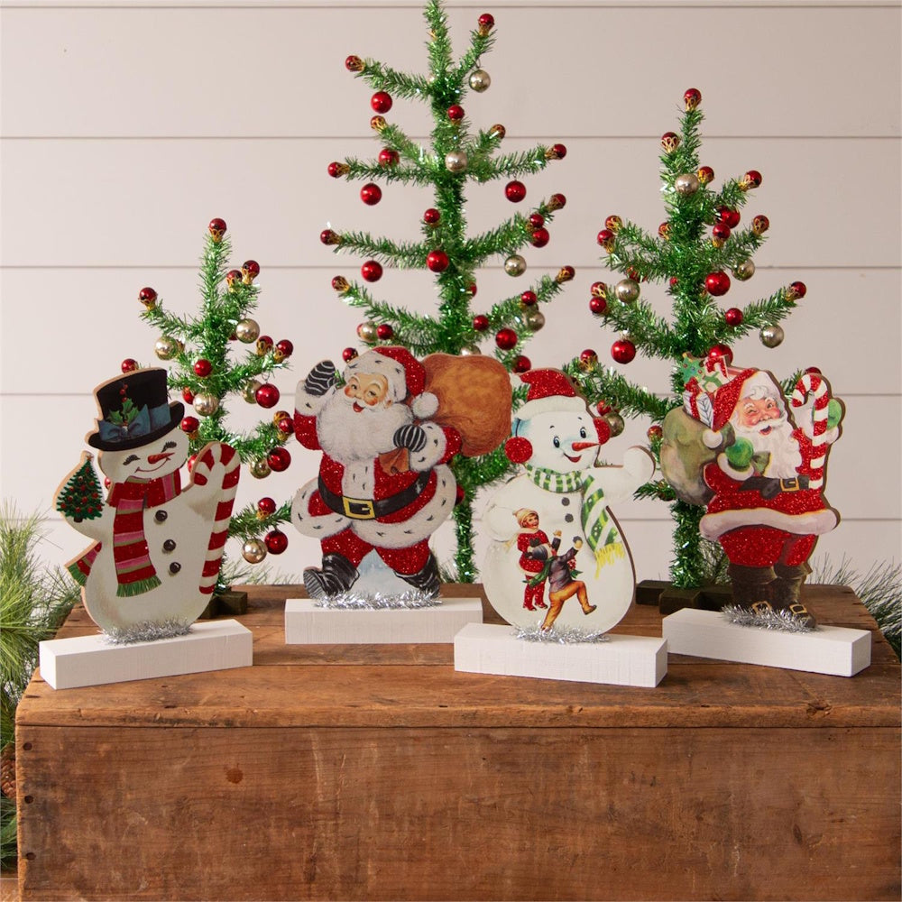 Vintage-style Santa and snowman tabletop cutouts displayed in front of miniature decorated trees.
