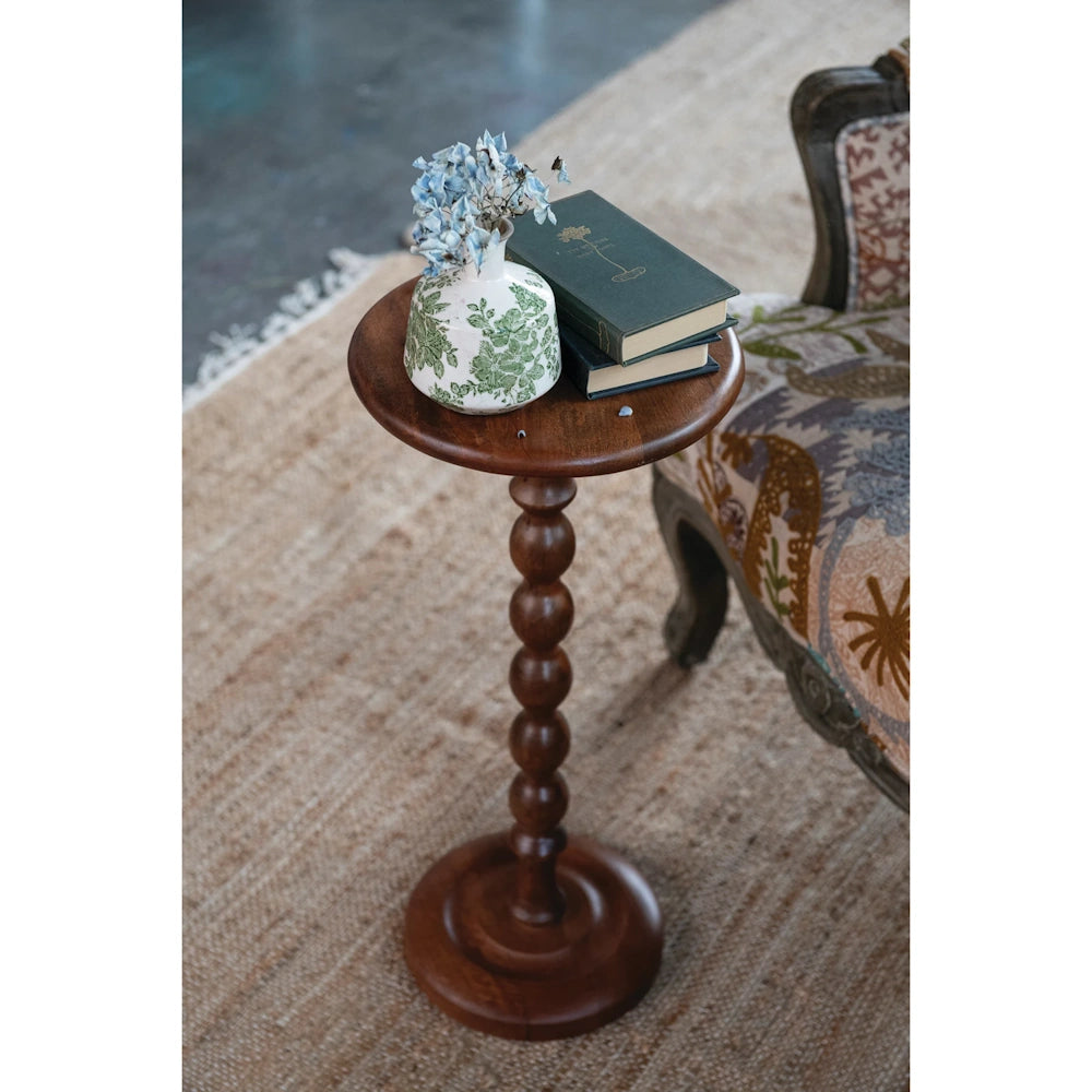 Dark wood turned-bead martini table next to an armchair holding two stacked books and a floral vase.