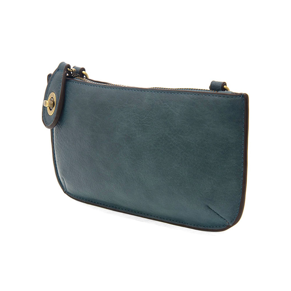 Washed denim blue leather mini crossbody wristlet clutch bag with brass hardware and zipper closure on a white background.