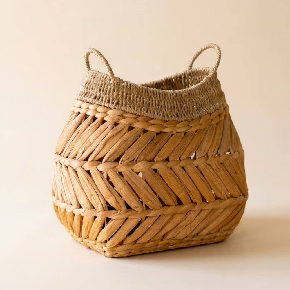 Handwoven water hyacinth storage basket with built-in handles against a neutral background.