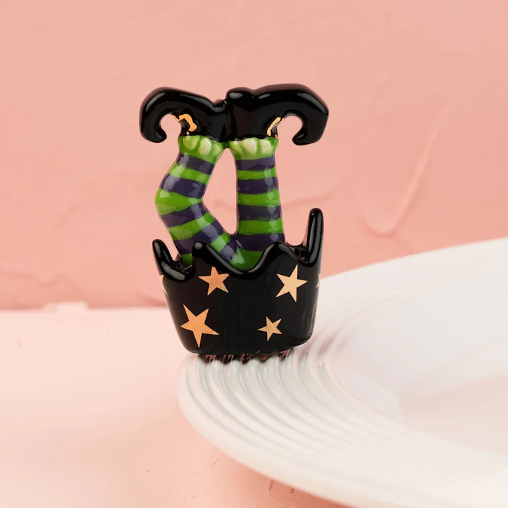 Ceramic figurine of upside-down witch legs in striped tights attached to the rim of a white plate.