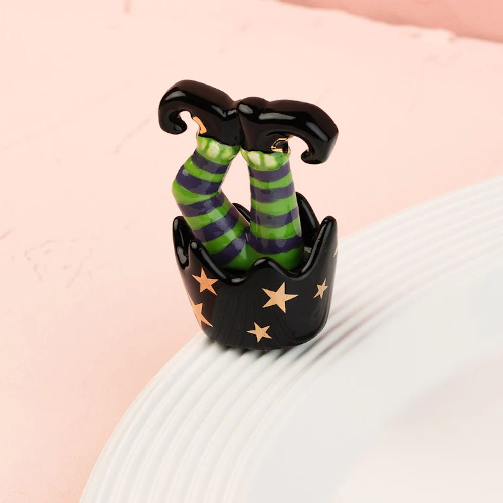 A small Halloween figurine of upside-down striped witch legs sticking out of a black, star-covered pot.