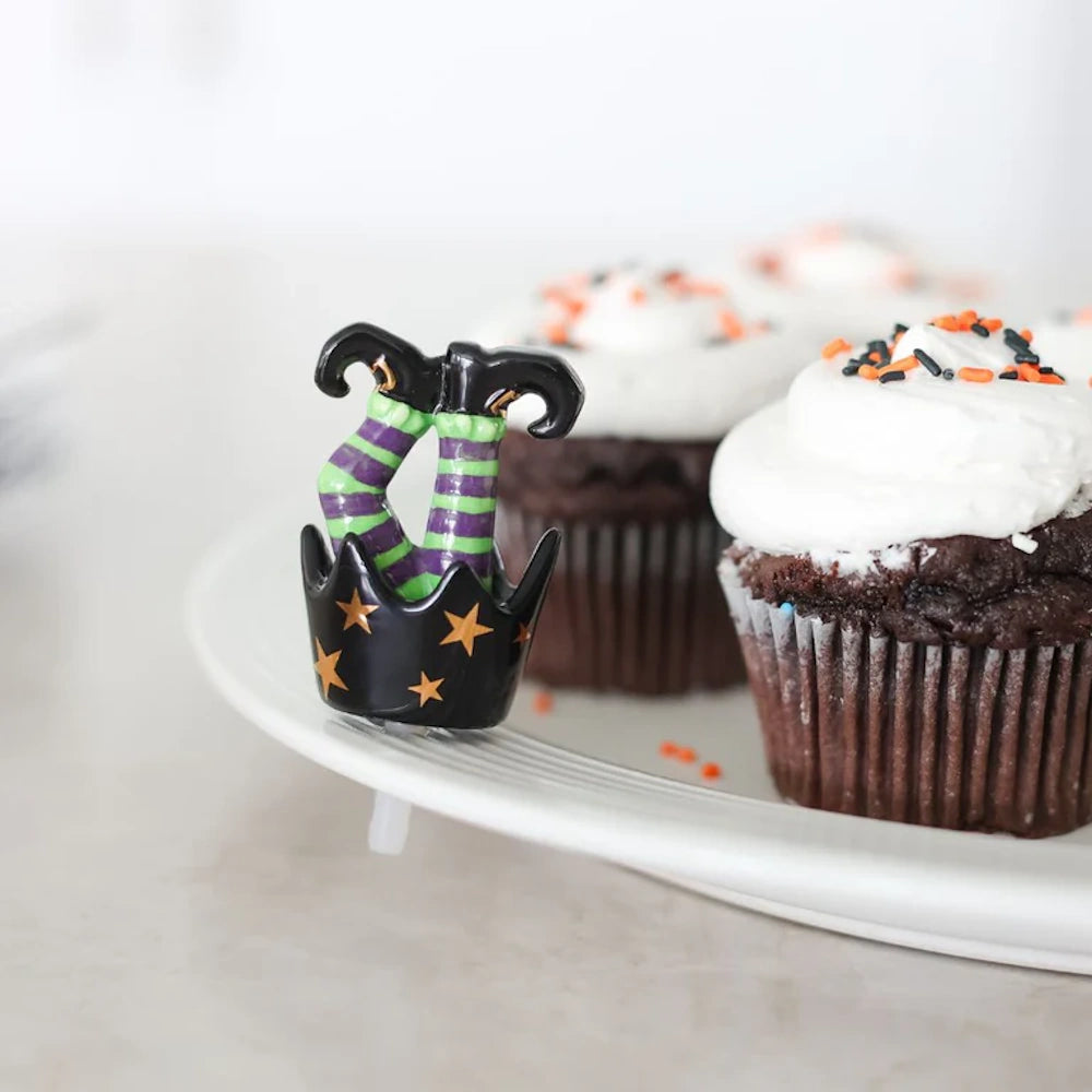 Striped witch legs decoration on a white platter next to frosted chocolate Halloween cupcakes.