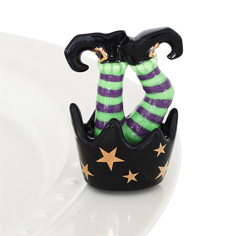 Ceramic upside-down witch legs with green and purple stripes in a black cauldron with gold stars.
