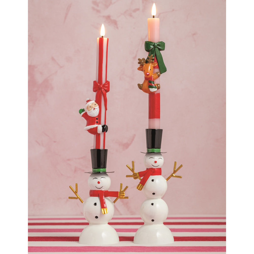 Lifestyle view of two lit taper candles in snowman holders, one with a Santa and one with a reindeer hugger.