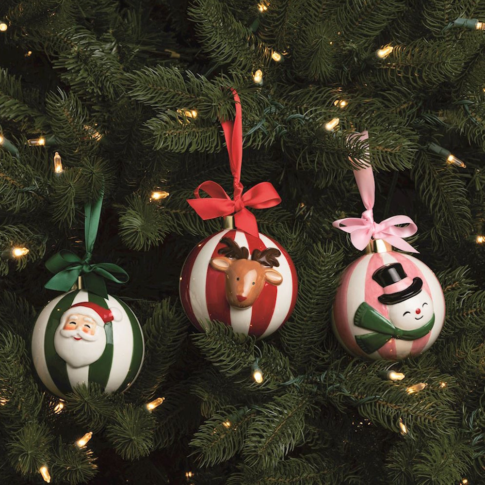 Three striped Christmas ball ornaments featuring Santa, a reindeer, and a snowman hanging on a tree.