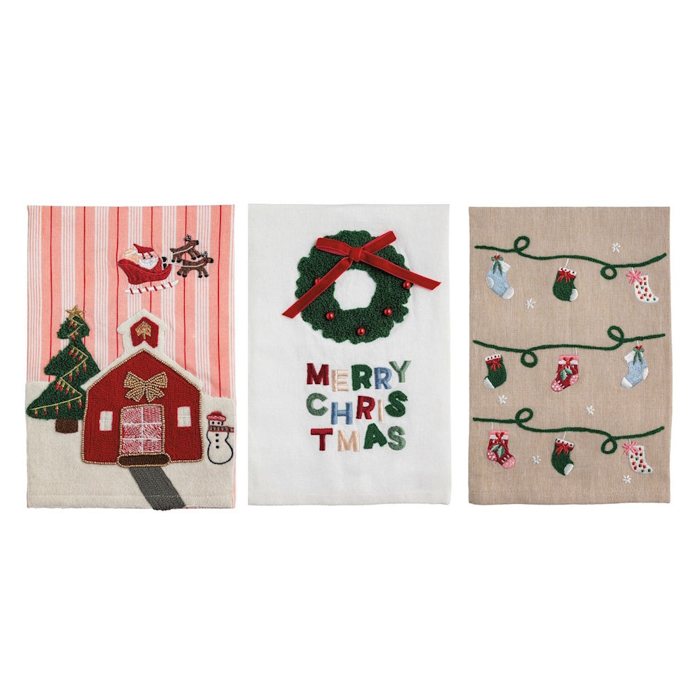 Set of three Christmas kitchen towels featuring a red striped barn design, a Merry Christmas wreath design, and a stocking garland design.