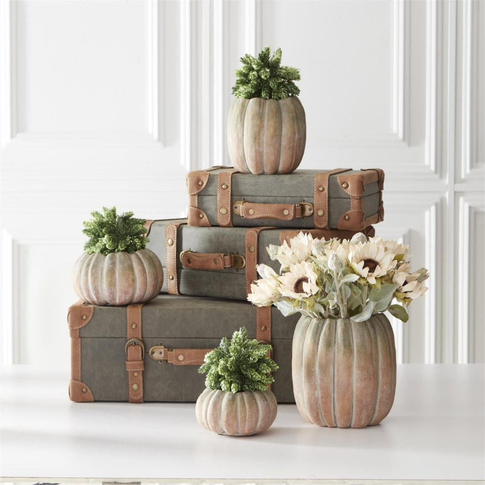 Stacked vintage suitcases with pumpkin-shaped planters holding greenery and a bouquet of cream sunflowers.
