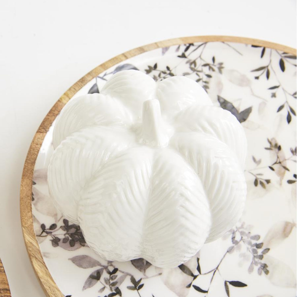 White ceramic chevron embossed pumpkin decor on a floral patterned wooden tray.