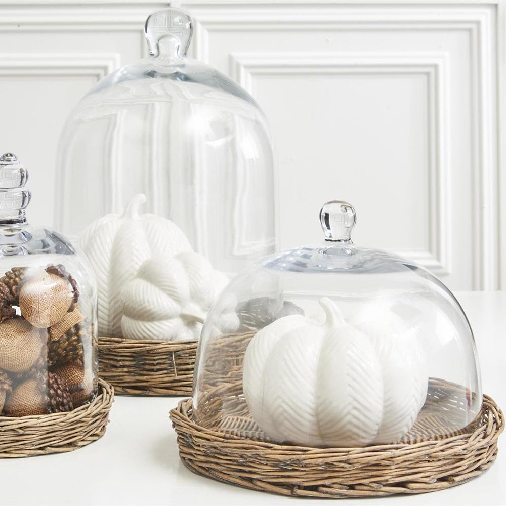 White ceramic pumpkins under glass cloches on woven trays for fall centerpiece decor.