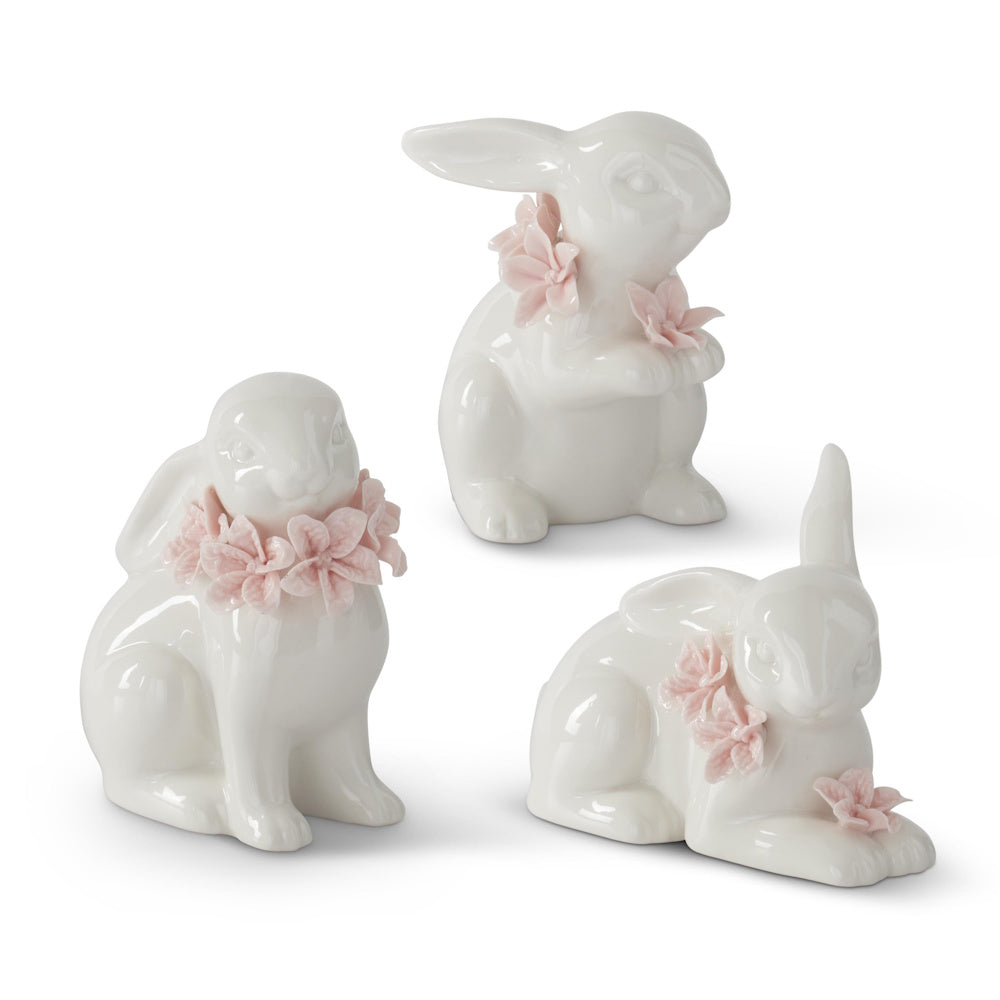 Three white ceramic Easter bunny figurines adorned with light pink floral collars and accents on a white background.