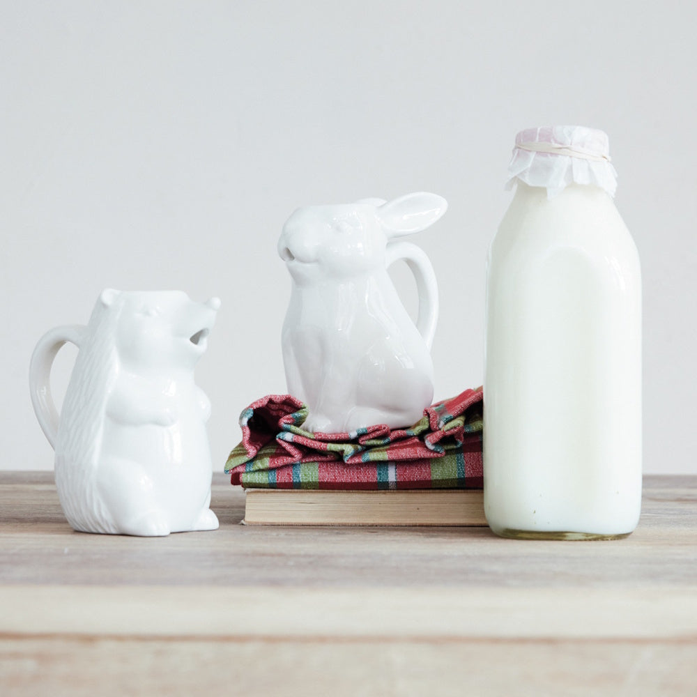 White ceramic animal-shaped creamer pitchers featuring a hedgehog and a rabbit next to a milk bottle.