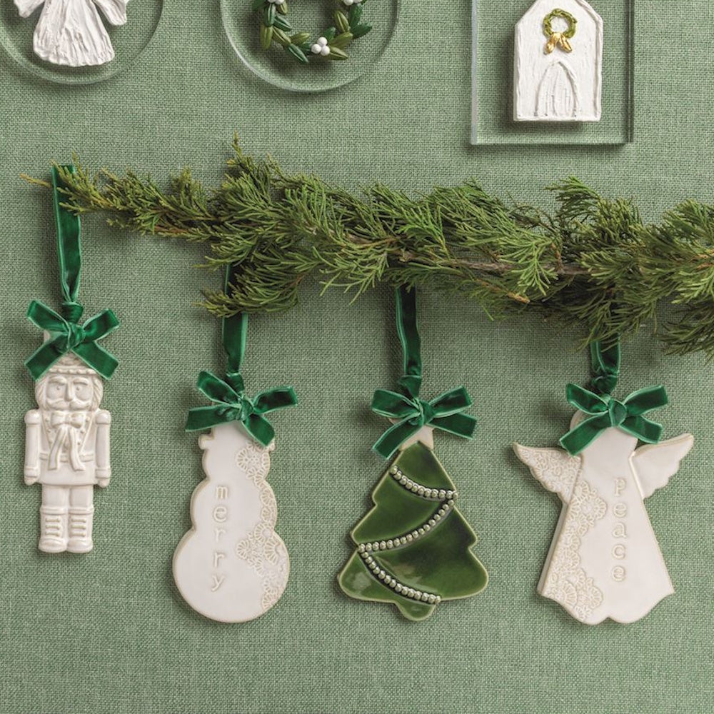 White and green ceramic Christmas ornaments with velvet ribbons hanging on an evergreen branch.