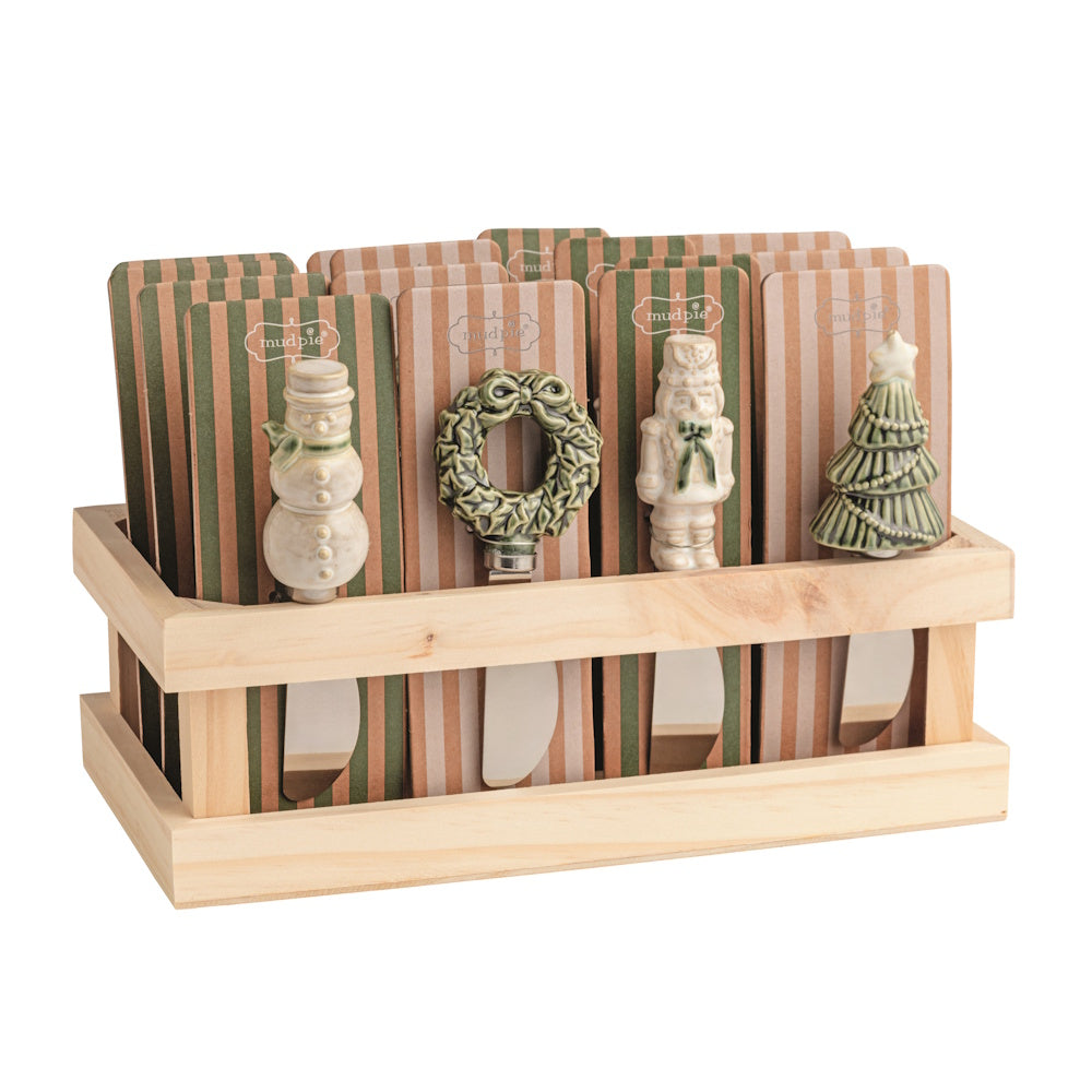 Wooden display crate filled with assorted white Christmas figural spreaders featuring a snowman, wreath, nutcracker, and tree.
