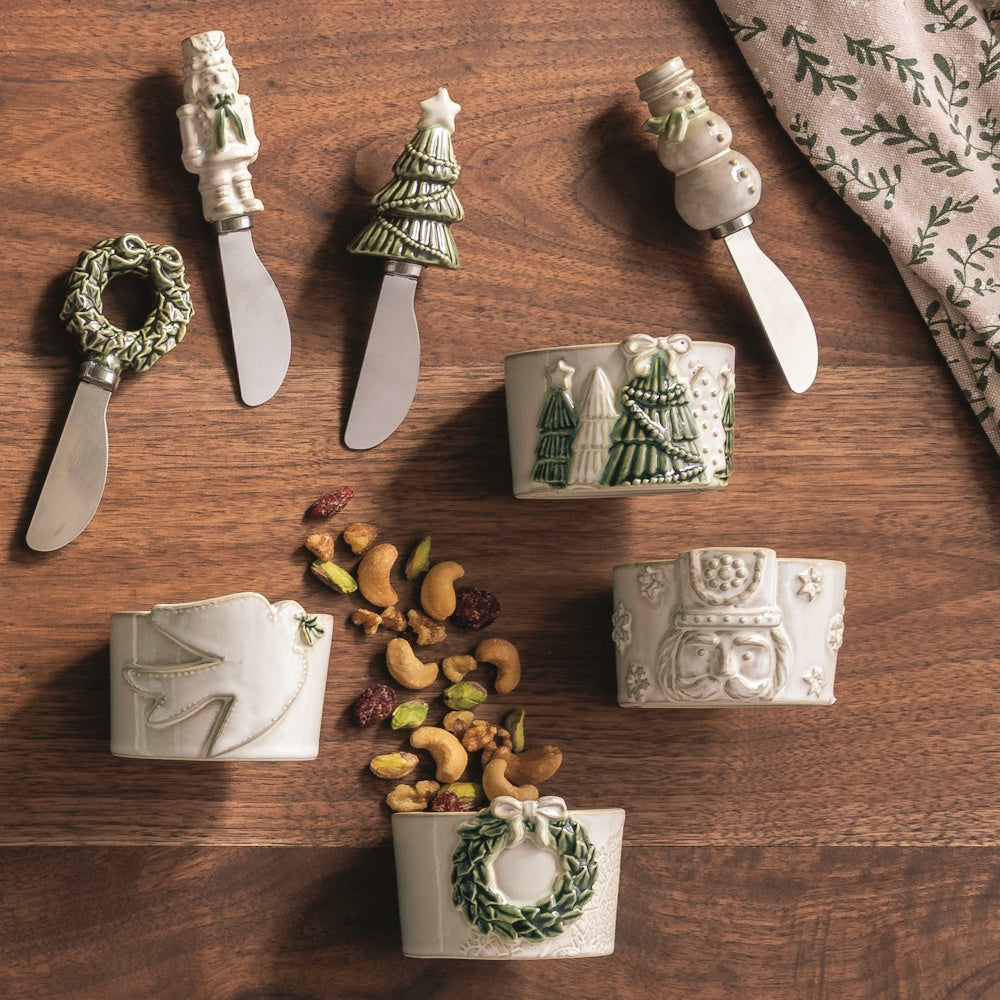 White Christmas figural spreaders and matching napkin rings arranged on a wooden table with nuts.