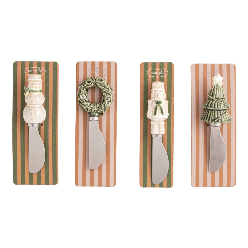 Four white Christmas figural spreaders featuring a snowman, wreath, nutcracker, and tree on striped packaging.