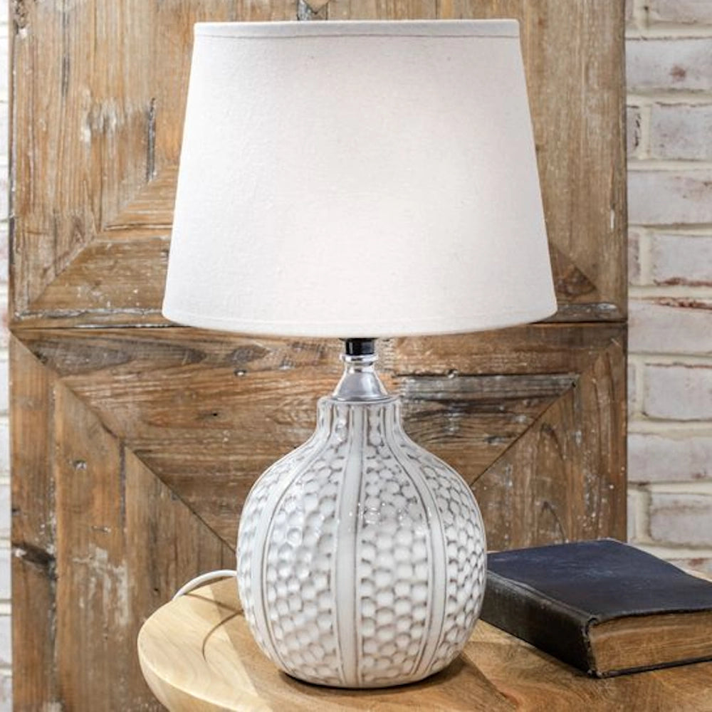 White textured dimple pattern ceramic table lamp with a cream tapered fabric shade on a wooden side table.