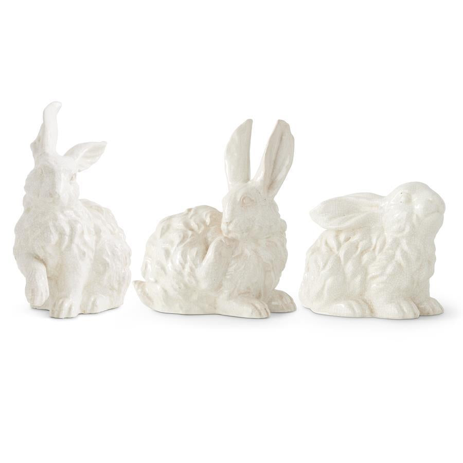 Three white glazed terracotta bunny figurines in various sitting and grooming poses on a white background.